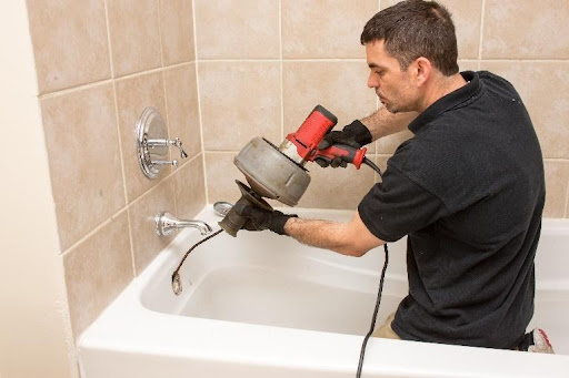 A plumber in the Greater Chicago Area performing a rooter service using an electric drain snake. A clogged bathtub in a residential home needing a rooter service.