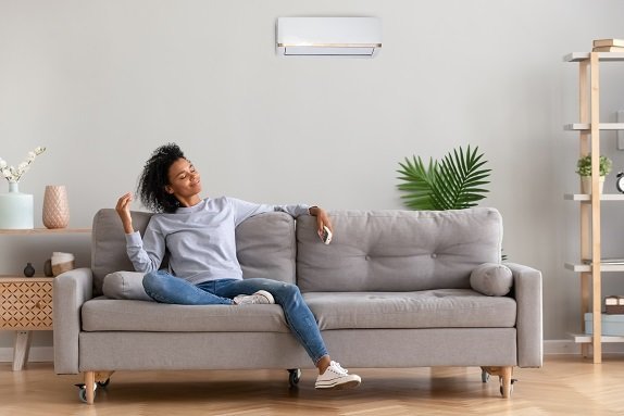 Woman sitting on gray couch in front of a ductless mini-split, looking comfortable.