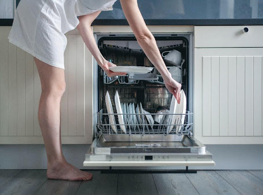 A female homeowner carefully loads her dishwasher in Carol Stream, IL, to ensure she is completing the process correctly.