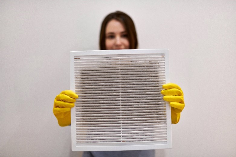 A young woman holding dirty and dusty ventilation grille in her home in Chicagoland.