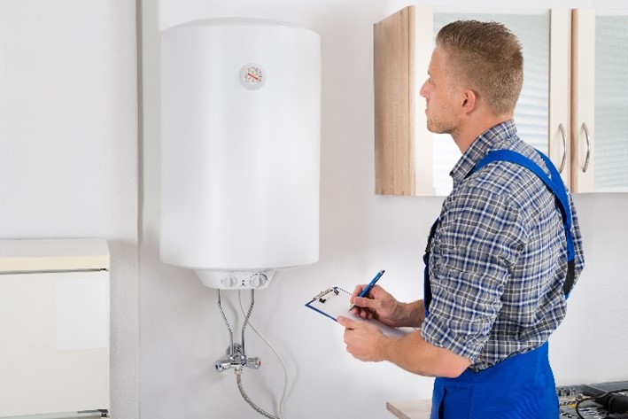 Professional technician in blue overalls with a clipboard examining a residential water heater in Carol Stream, IL.