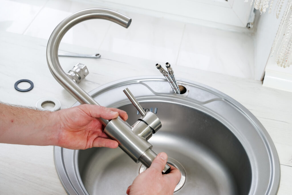 Plumber hands holding a new brushed nickel faucet for installing in a kitchen sink
