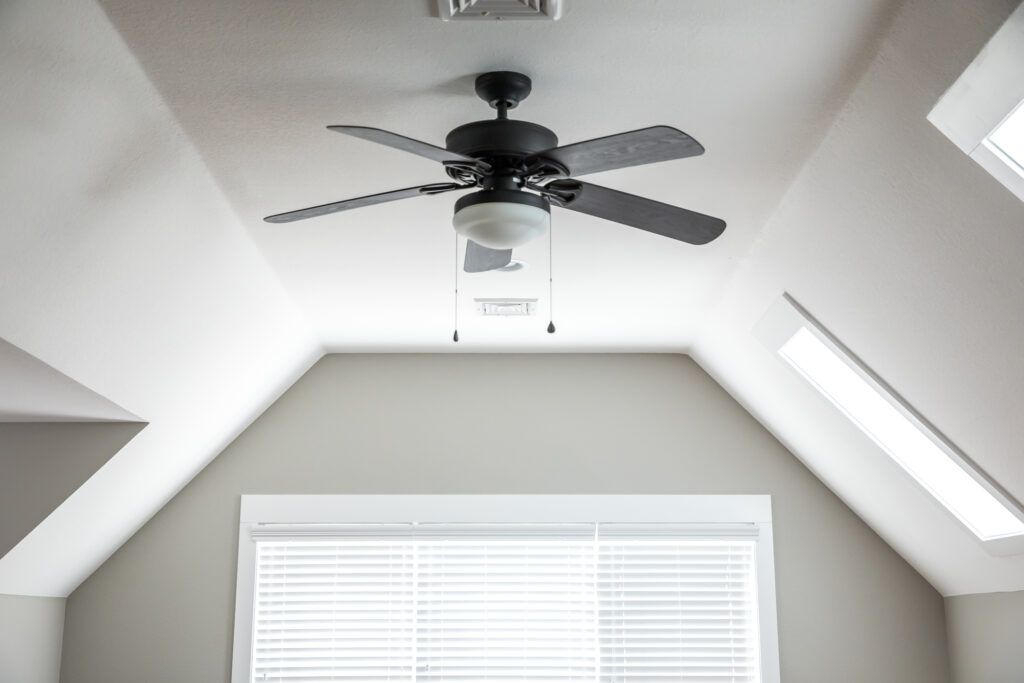 Open and airy bonus room in a new construction house with a dark wood ceiling fan, a window and blinds. White walls.