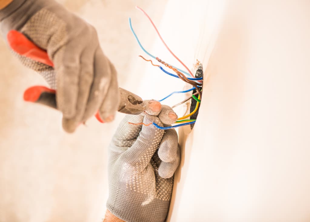 Close view of gloved electrician's hands as they snip electrical wires.