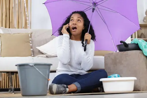A homeowner is experiencing a burst pipe in her Chicago, IL, home so she is using buckets to catch the water and an umbrella to keep herself dry.