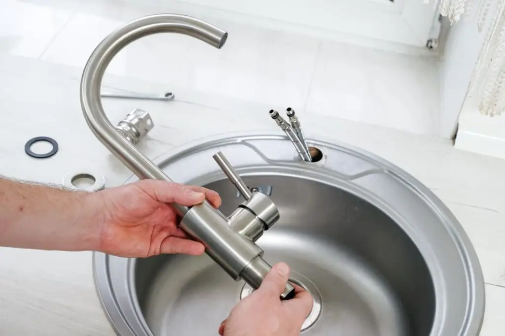 Plumber hands holding a new brushed nickel faucet for installing in a kitchen sink